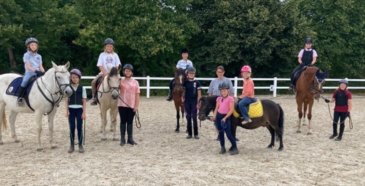 Gruppe von Kindern auf Schulpferden und Ponys, aufgereiht auf dem Reitplatz